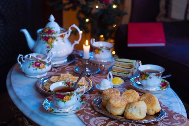 Candlelit tea scene with china, cookies, scones, and sandwiches with Christmas decorations