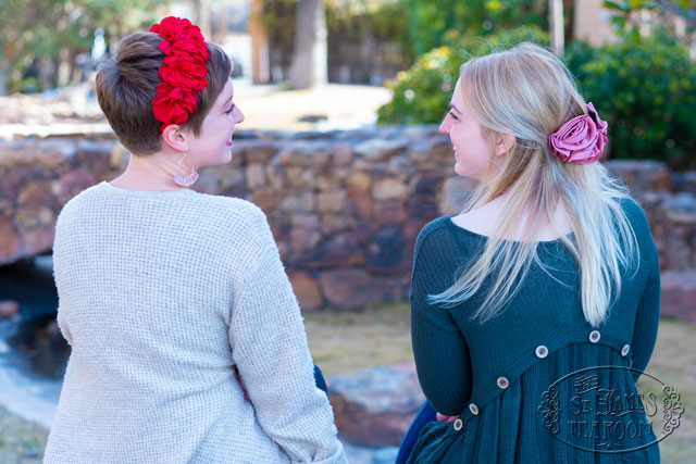 Two women sit together outside with flower hair accessories